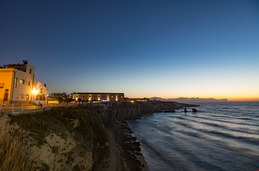 Il lungomare di Terrasini al crepuscolo: le luci del paese sulla scogliera e il mare aperto verso l'orizzonte